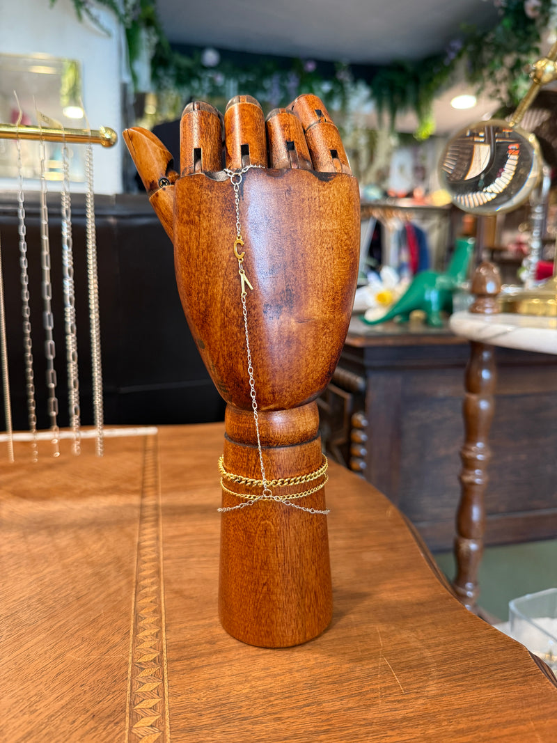 Permanent jewelry chains displayed on a wooden hand inside The College Artisans Shop
